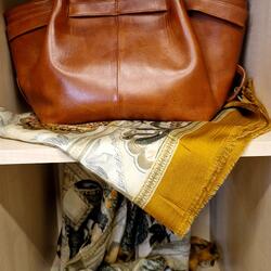 Braune Ledertasche auf gemusterten Tüchern im Regal
